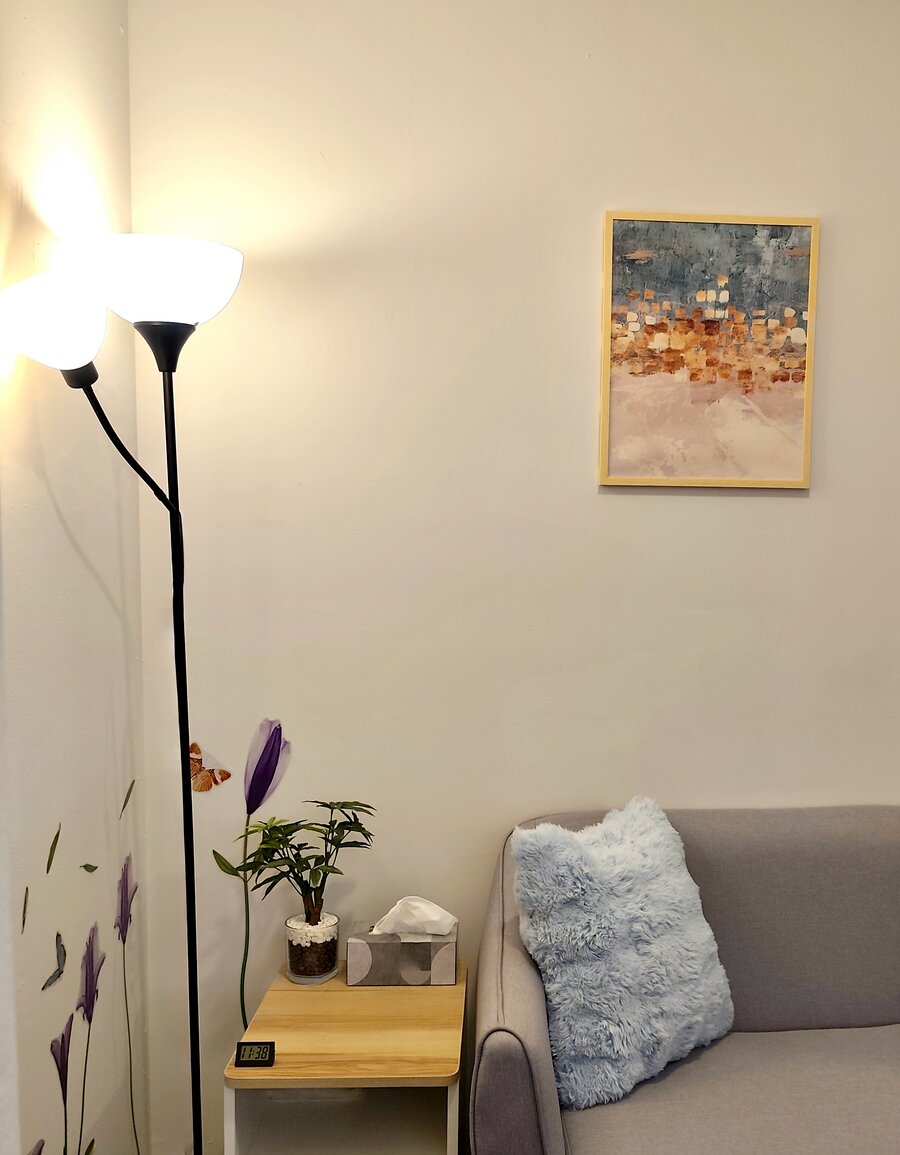 A warm corner of the counselling room, with a floor lamp, plant and soft cushion